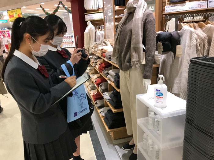 2人がペアになって店舗を訪問し、入り口付近の消毒液の設置場所を確認して写真に記録しています。